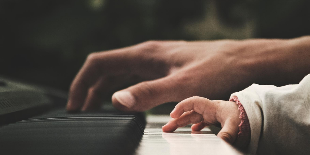 adult hand with young childs hand on piano keys