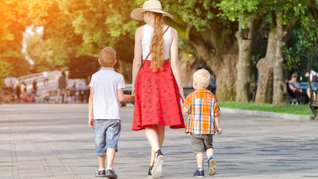 Mum looking stylish walking away down a road holding the hands of her two kids