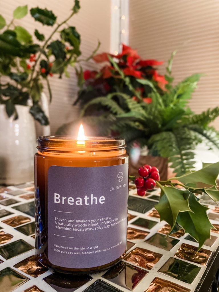Breathe aromatherapy candle lit with holly in the background.
