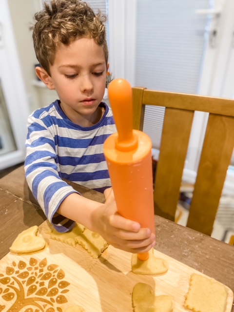 Boy using rolling pin to make a small indent in the shortcake biscuits dough