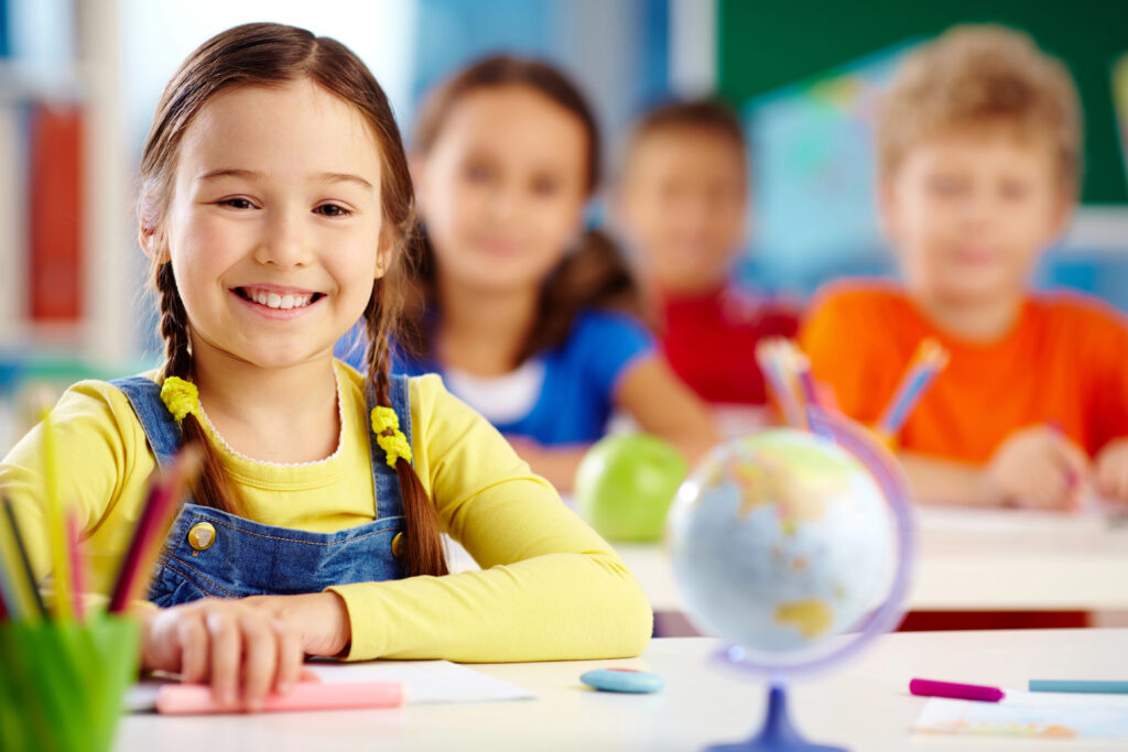 Child at her desk at school smiling and happy with a small world glove by her