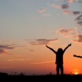Two kids reaching their arms out to the sky with the sunset behind them - enjoying life!