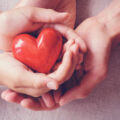Two pairs of hands holding a red heart