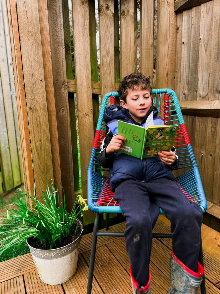 Boy in his garden reading a book about spring next to a pot of daffodils
