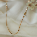 Minimalist gold necklace laying on white satin by white flowers