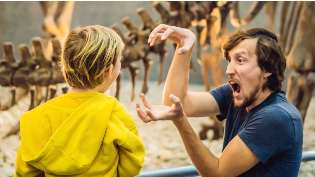 A dad on a day out at the museum with his kid pretentding to be a dinosaur in front of dinosaur bones