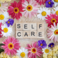 Self care spelt out in scrable blocks with flowers surrounding it