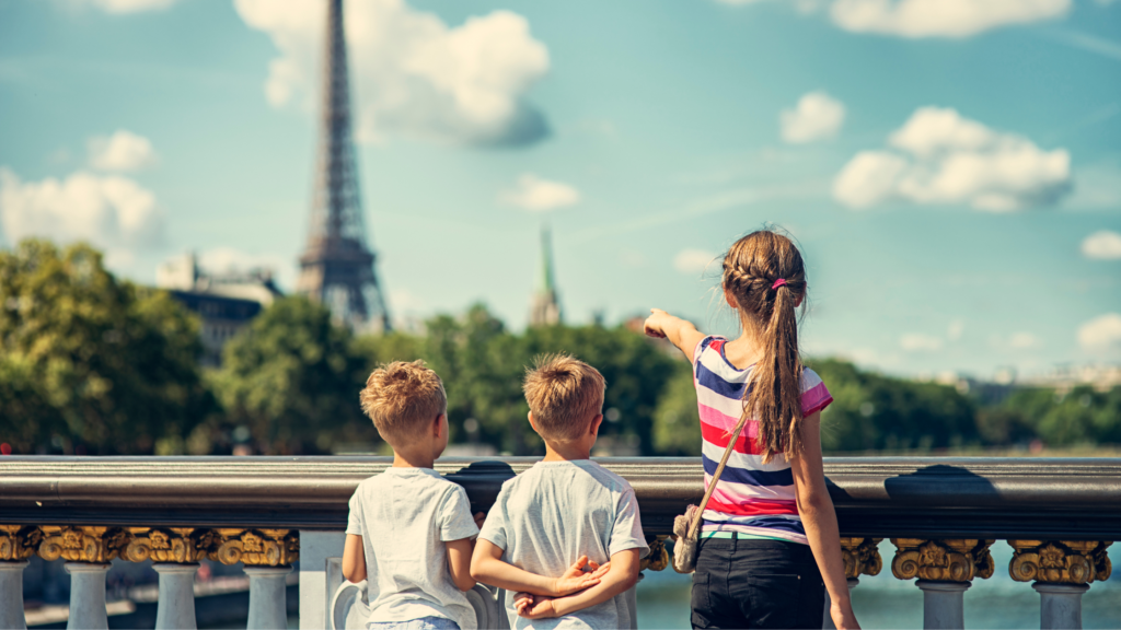 Three children in Paris pointing at the Eiffel Tower from the Pont Alexandre III