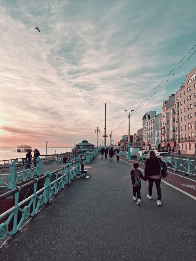 Mum and son walking along the seafront in Brighton with the i360 in the distance and the sun setting