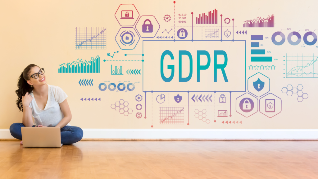 GDPR written in green on the wall with interlinking info and graphics. Woman sitting on the floor with laptop on her lap looking at the writing on the wall.