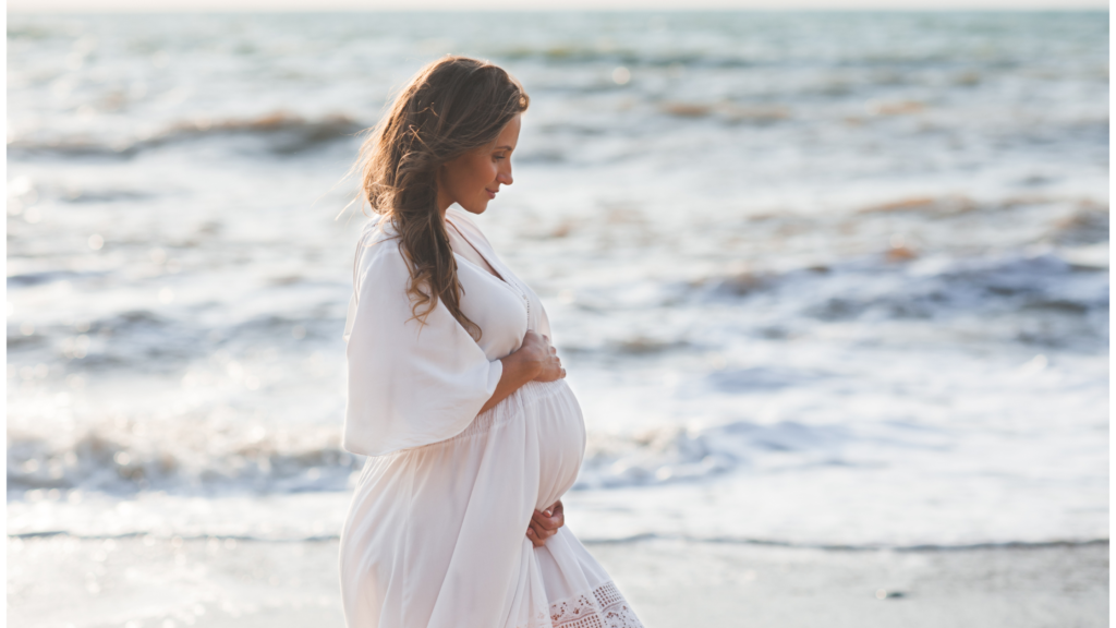 Pregnant lady on the beach in loose stretchy white linen and cotton.