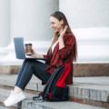 Lady sitting on the steps of a tourist attraction with her laptop and a coffee, working to make money whilst she travels.