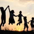 Silhoutes of children jumping for joy at sunset in a meadow.