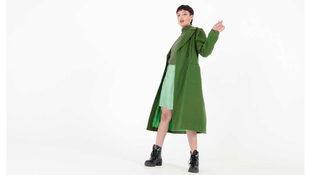 Lady with short hair in a long forest green coat and light forest pallette skirt