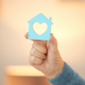 Blue cut out house with a heart in the middle being help by a hand to represent a care home