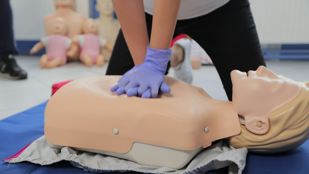 Hands shown in purple medical gloves pressing down on a resussatation doll practicing cpr