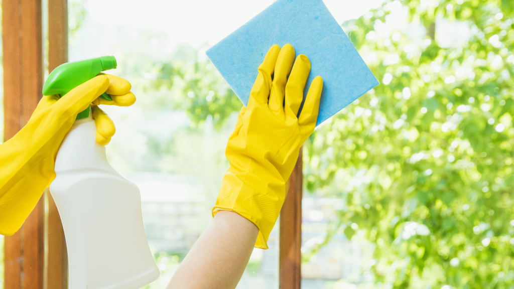 Hands in yellow rubber gloves cleaning with a blue cloth the windows