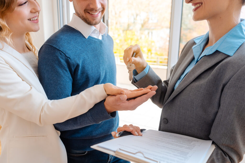 Realtor woman giving house keys to couple, closeup of hands