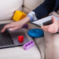 The hands of a mum trying to work on her laptop surrounded by baby and toddler tous.
