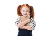 Young girl with red hair in bunched holding a school book with a happy expression on her face