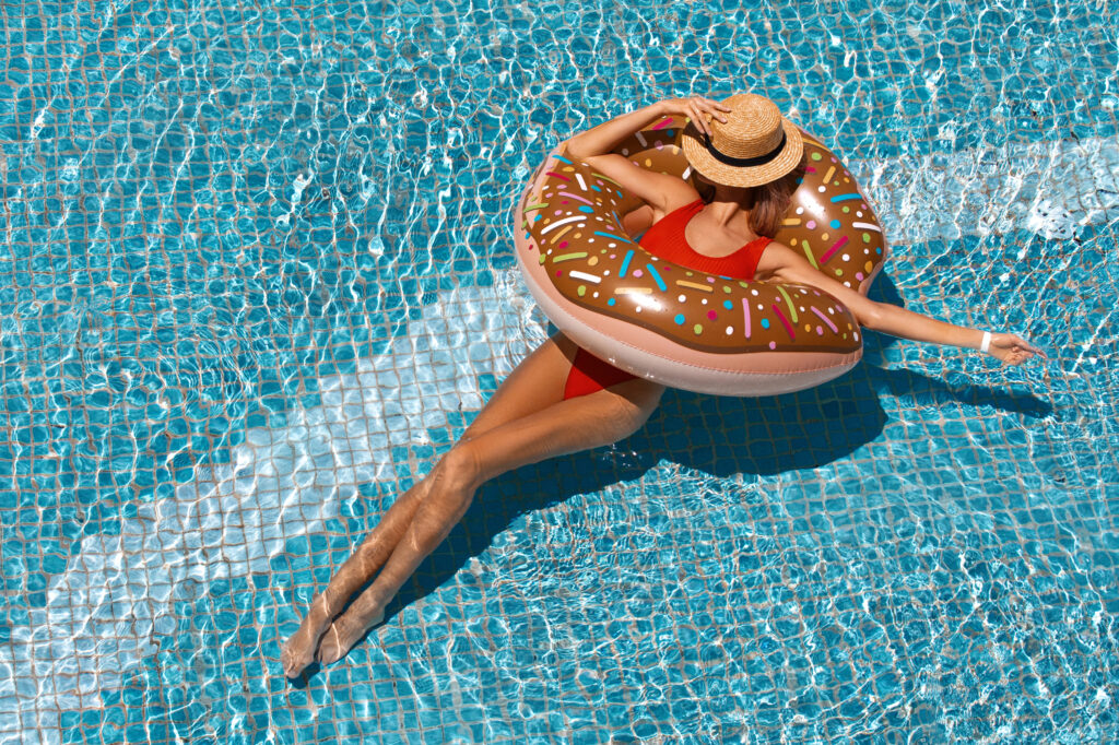 Lady in a swimming pool with red swimwear and sun hat in a donut inflatable