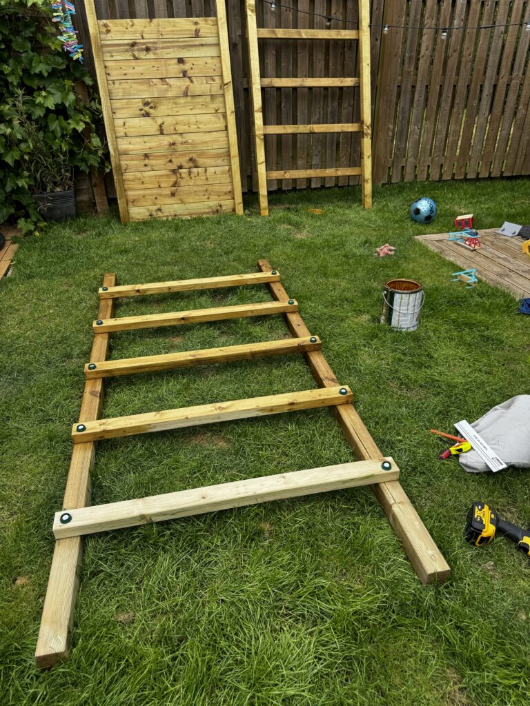 Assembing the Wickey Climbing Tower with side panel and ladder on the grass and leaning up against the fence
