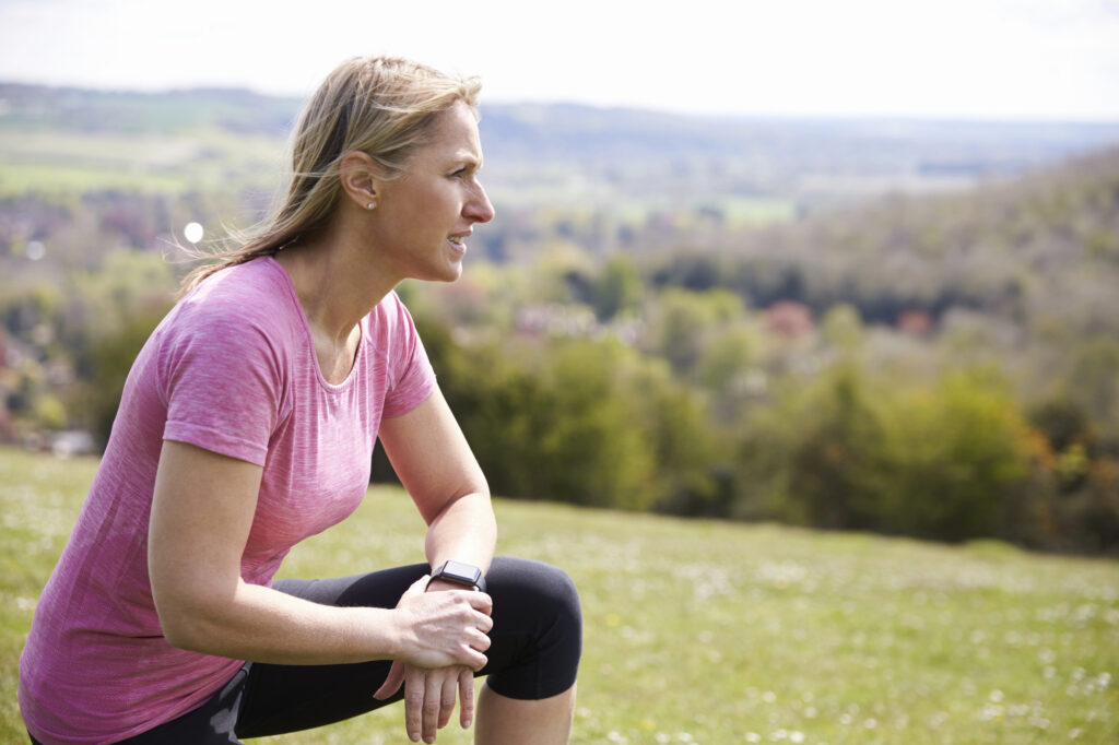 Woman in pink workout top and blacl leggings resting during her exercise outside
