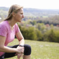 Woman in pink workout top and blacl leggings resting during her exercise outside