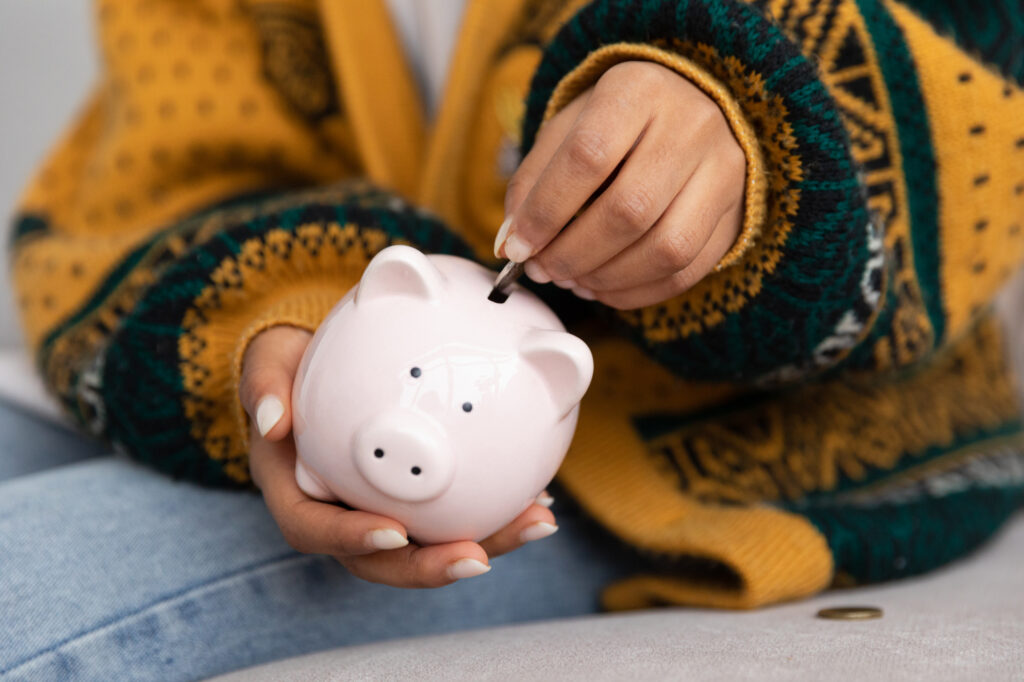 Womans hand putting a coin into a piggy bank to represent saving and budgeting