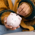 Womans hand putting a coin into a piggy bank to represent saving and budgeting