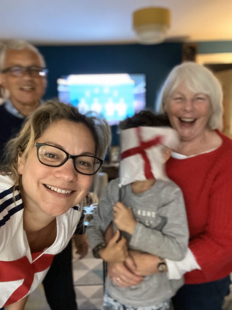 A group of people of three generations posing for a photo with an England flag watching an English live football game at home