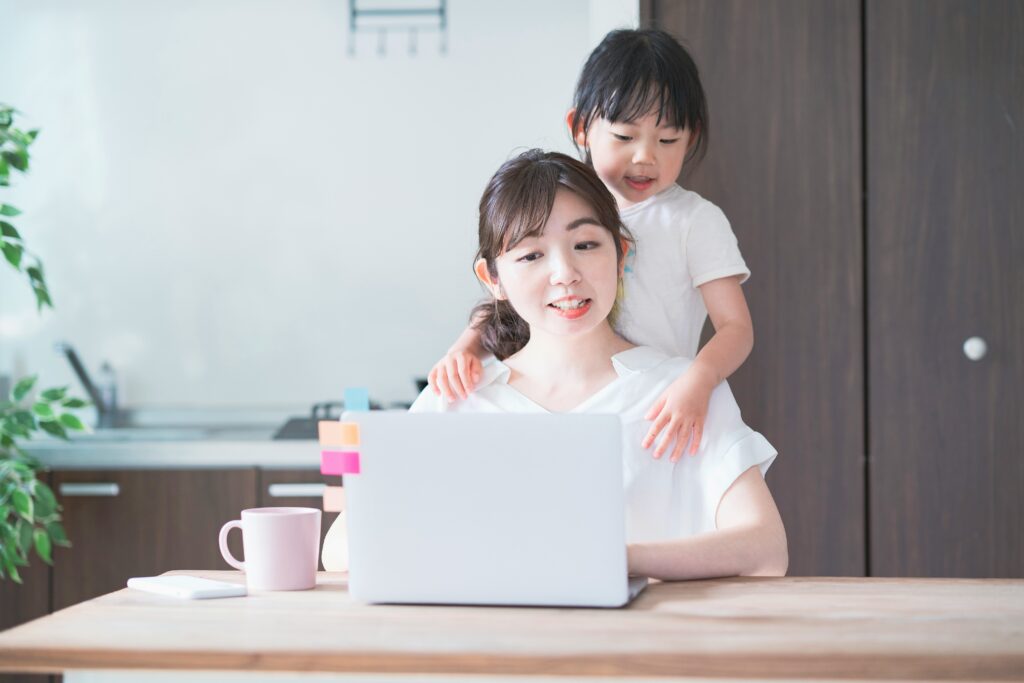 Cute little girl hugging her mum from behind as her mum works on the laptop