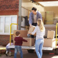 Family moving house outside the moving van loading boxes with young boy and mum passing boxes up to dad in the van