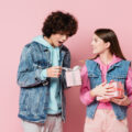 Teenage girl and teenage boy with a gift each with a pink background to represent a blog post for gifts for teens for Christmas