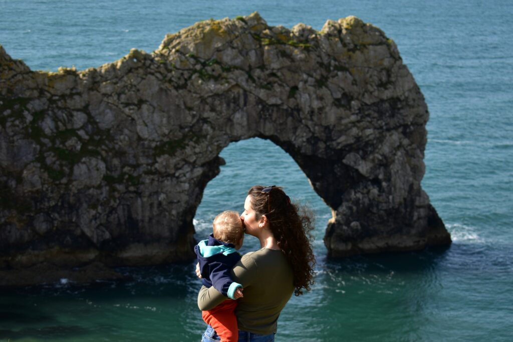 Woman kissing her baby whilst looking down at the arch of Durdle Door in Dorset
