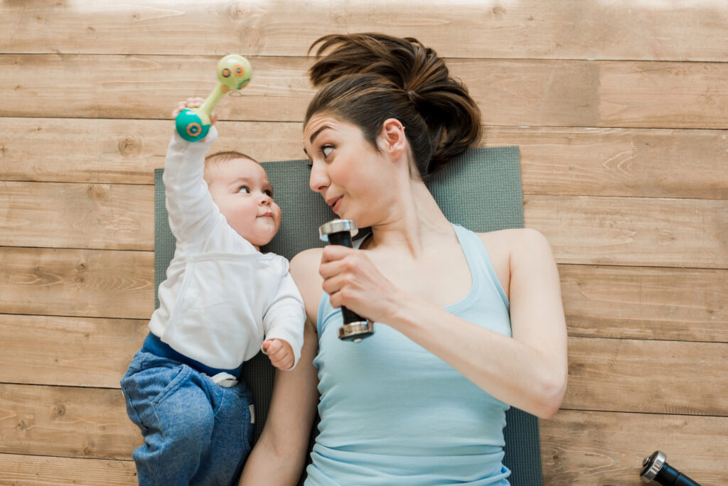 Mum with her baby lying on the floor on a yoga mat holding a dumbbell