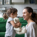Mum and young daughter playing in their home with daughter's white teddy bear