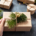 Woman's hand holding Christmas present wrapped in brown paper and string and garnished with fir tree branch and gold bauble