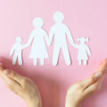 Woman's hands protecting paper family on pink