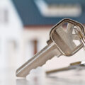 Keys with blurred house in the background to illustrate new home.
