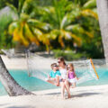 Mother and two children on a hammock on a white sandy beach whilst on a beach vacation
