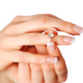 A ladies hands featured with white background as she slips on her diamond ring