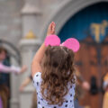 Little girl from behind with pink mickey ears dancing to the princess parade at Magic Kingdom by the castle in Orlando Florida