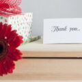 A notes saying thank you next to a wrapped parcel with red flower