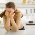 Woman stressed in kitchen holding her head in her hands