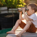 Boy sitting on a bridge looking through binoculars