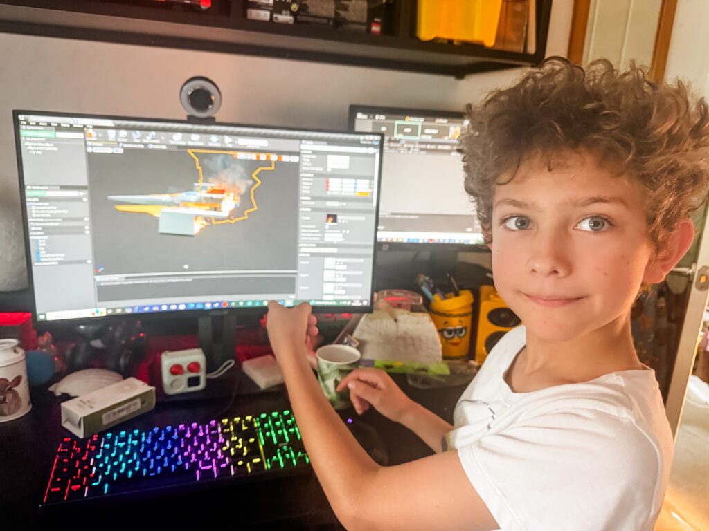 A boy pointing at his spaceship on his computer monitor on his 3d game design course for kids