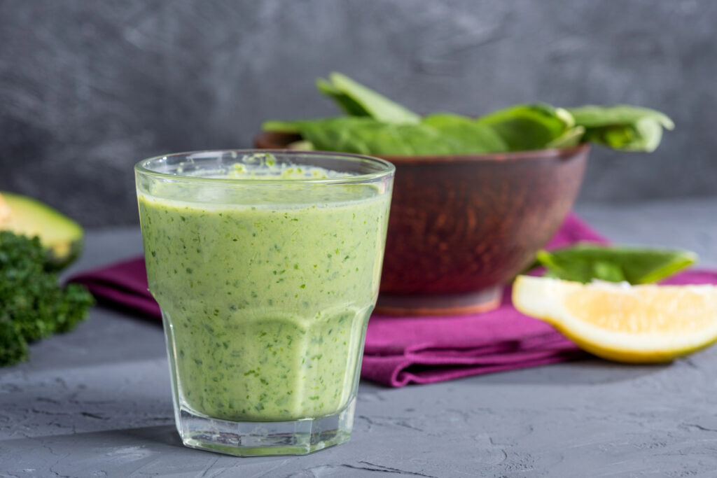 A healthy green smoothie in front of a bowl of healthy food