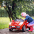 Little girl next to her red ride on car