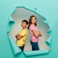 Boy and girl standing back to back behind a torn blue screen to show their independence and confidence